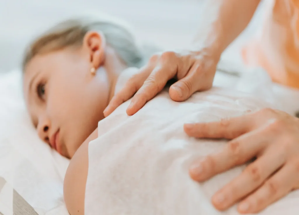 Dłoń terapeuty pracująca delikatnie na plecach leżącego dziecka podczas wizyty osteopatycznej